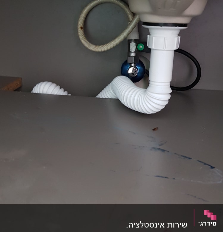 צינור פלסטיק לבן מתחת לכיור עם ברז סגירה